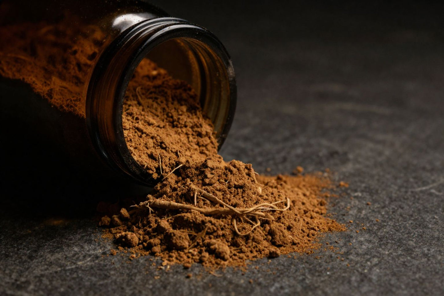 Dramatic close-up of ashwagandha root powder spilling from a dark glass jar onto a stone surface, deep amber and shadow tones, cinematic health editorial photography